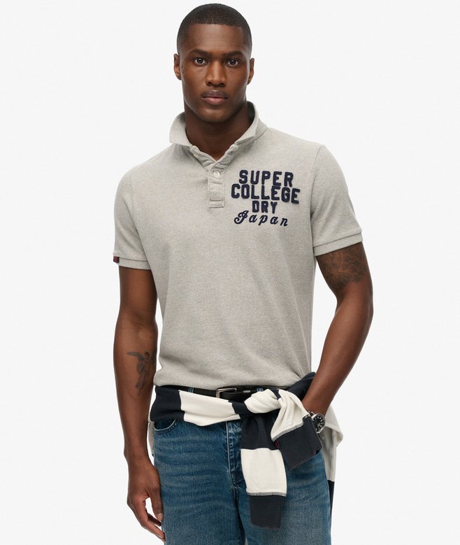 Man wearing a gray polo shirt with text and blue jeans on a white background