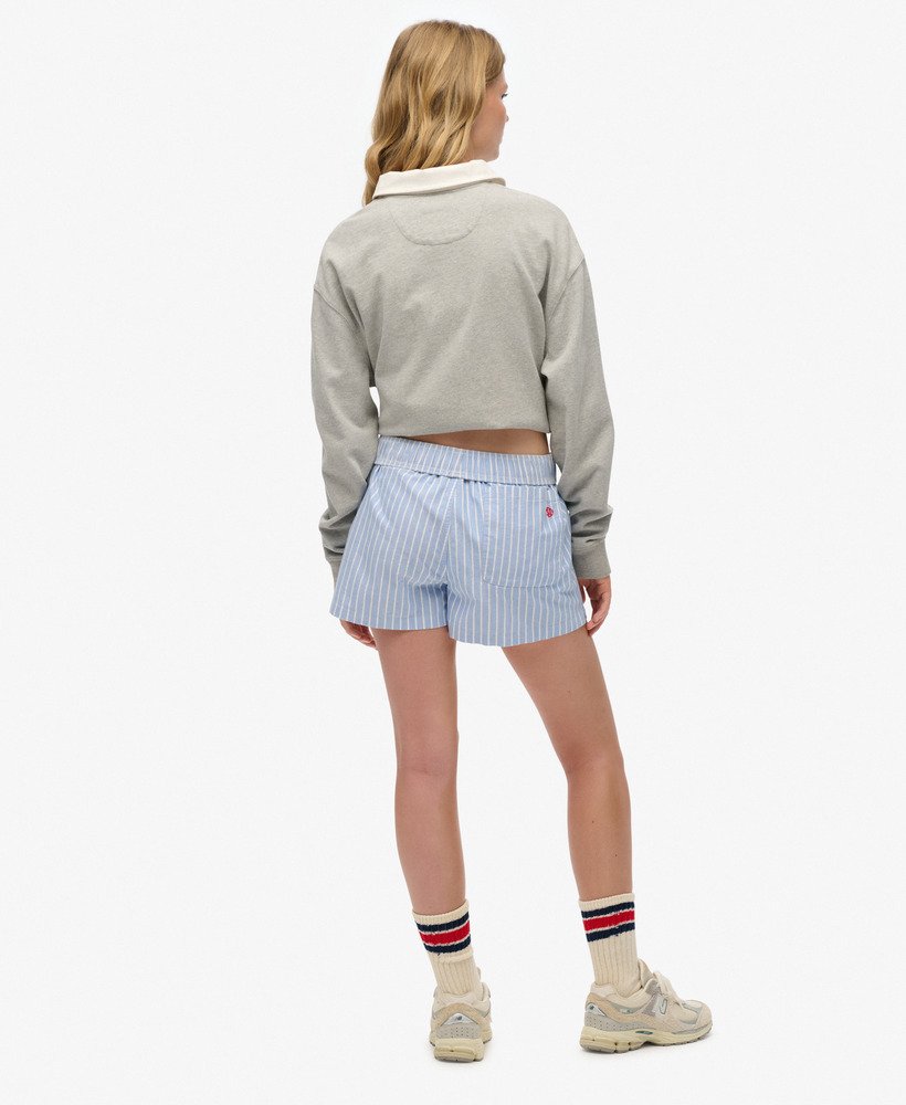 Person wearing a gray cropped sweater and blue striped shorts on a white background