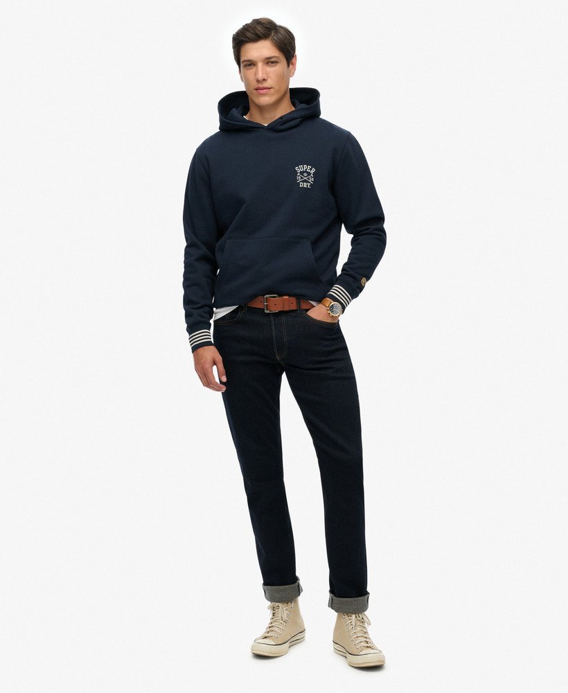 Man wearing a navy hoodie and dark jeans on a white background