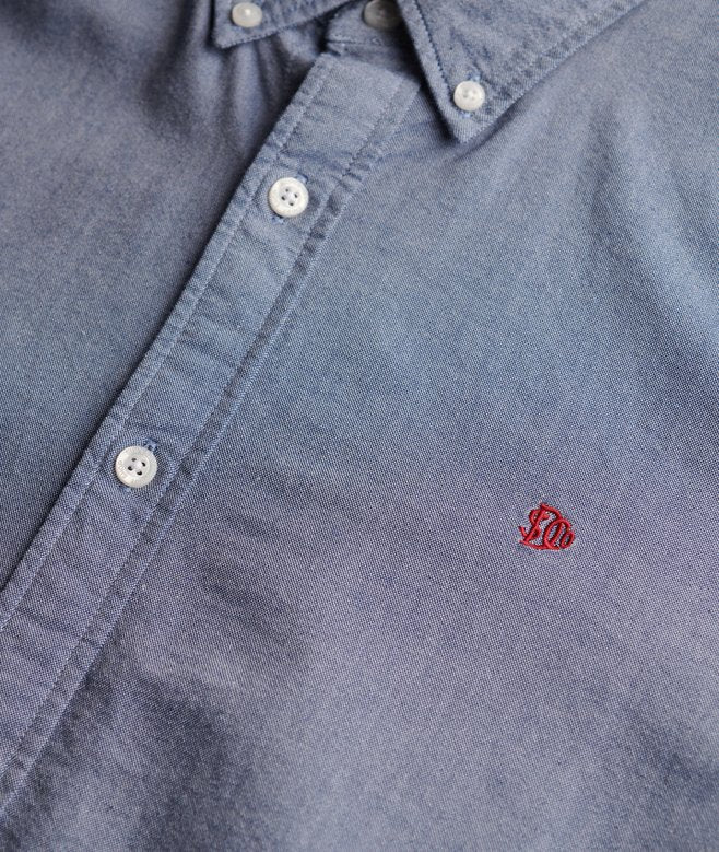 Close-up of a blue shirt with a red logo on the chest pocket.