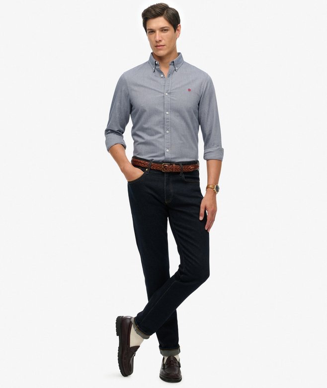 Man wearing a blue button-up shirt and black pants on a white background