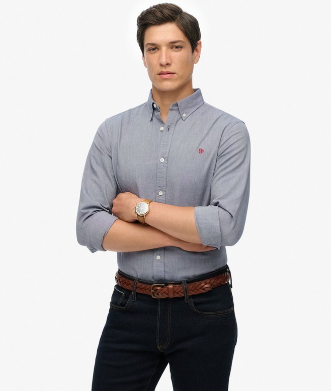Man wearing a blue button-up shirt and dark jeans on a white background