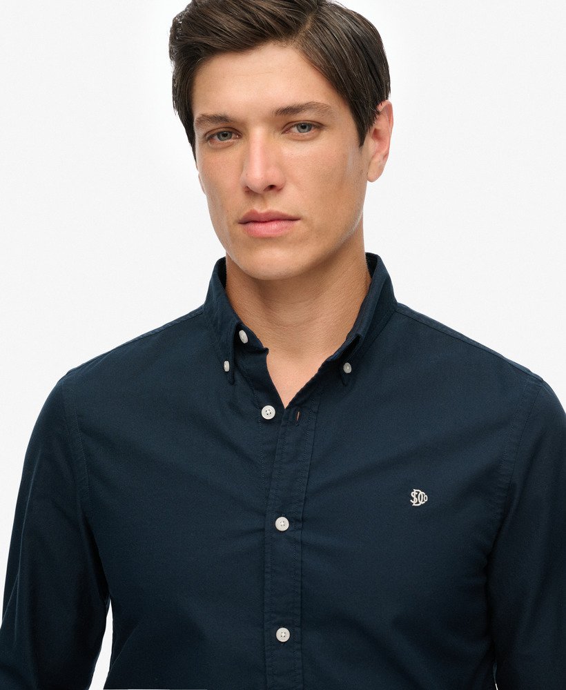Man wearing a navy button-up shirt with a small logo on a white background