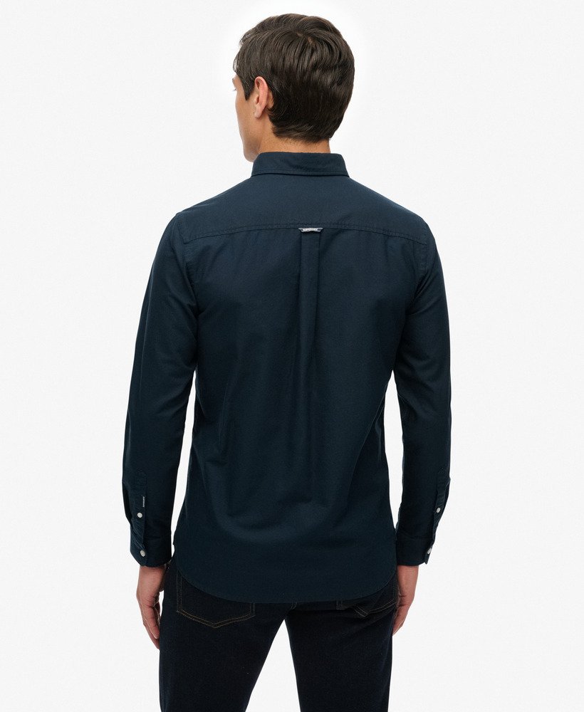 Man wearing a dark blue shirt with a visible brand logo on the back against a white background