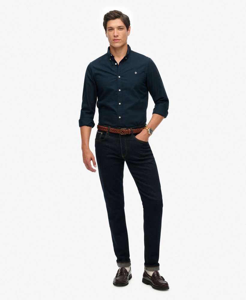 Man wearing a navy button-up shirt and black pants on a white background