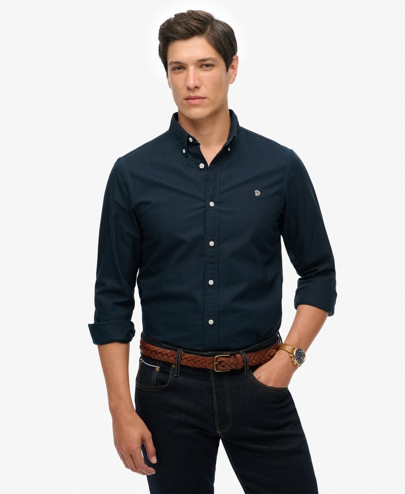 Man wearing a navy button-up shirt and dark jeans on a white background
