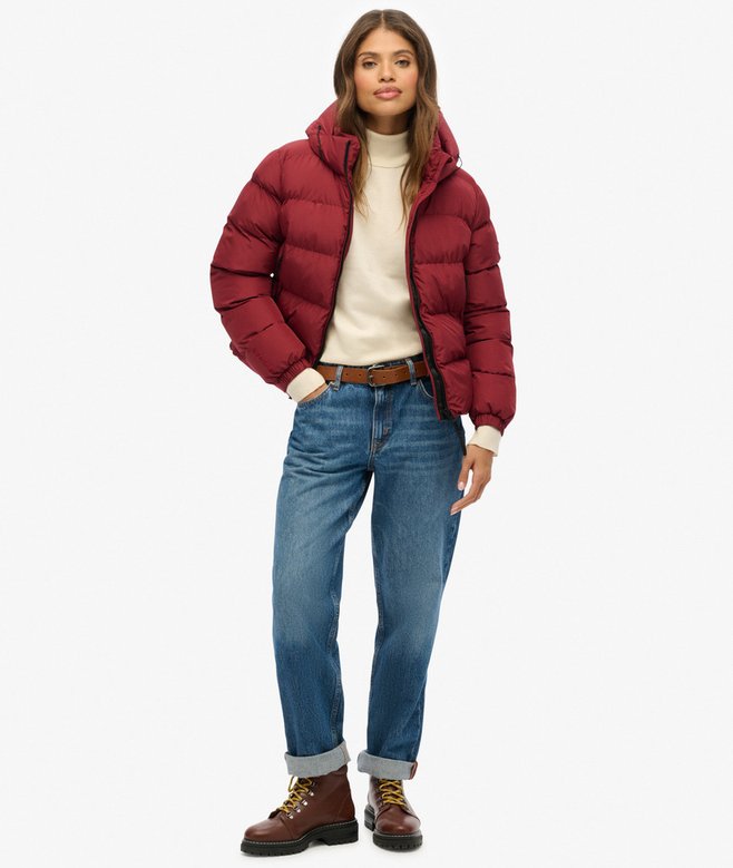 Woman wearing a red puffer jacket, white sweater, blue jeans, and brown boots on a white background