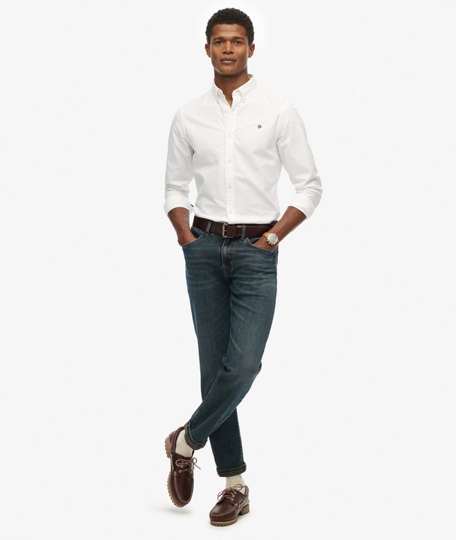 Man wearing a white dress shirt, dark jeans, and brown shoes on a white background