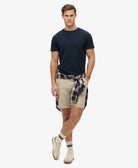 Man wearing a navy t-shirt, beige shorts with a plaid pattern, and white sneakers on a white background