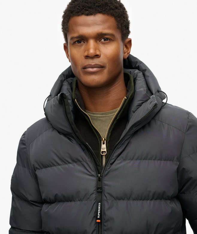 Man wearing a dark gray puffer jacket with a brand logo on a white background