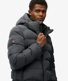 Man wearing a gray puffer jacket with a visible brand logo on a white background