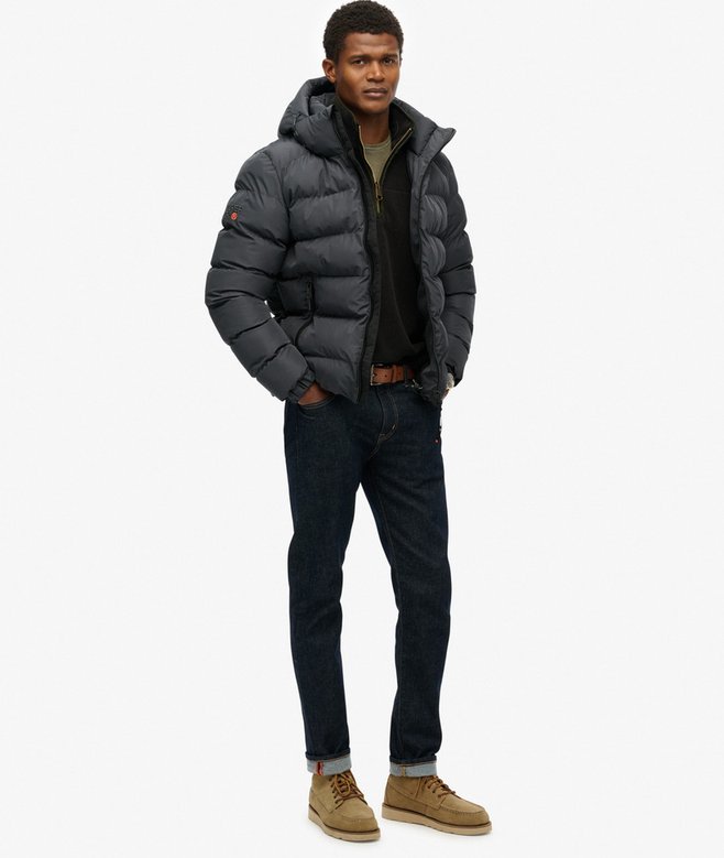Man wearing a grey puffer jacket, dark jeans, and brown boots on a white background
