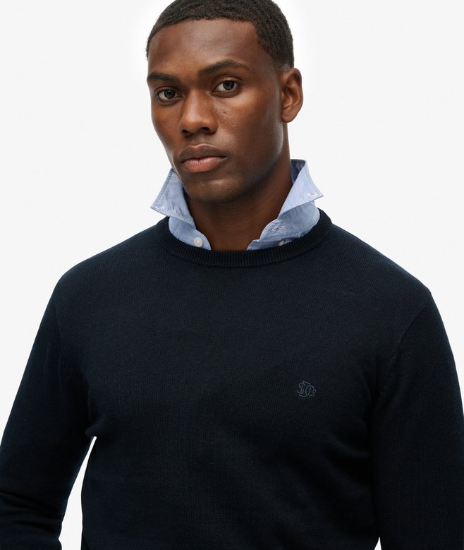 Man wearing a navy sweater over a light blue shirt on a white background
