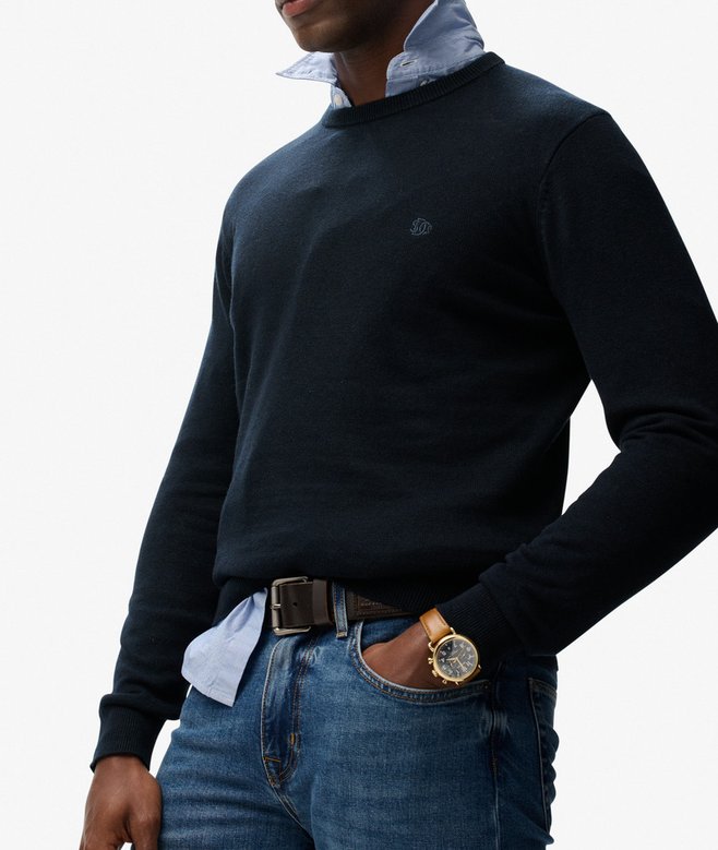 Man wearing a navy sweater over a light shirt with blue jeans on a white background