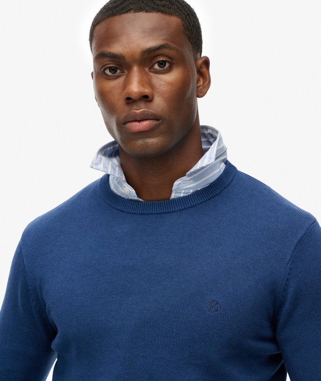 Man wearing a blue sweater with a white collar against a light gray background