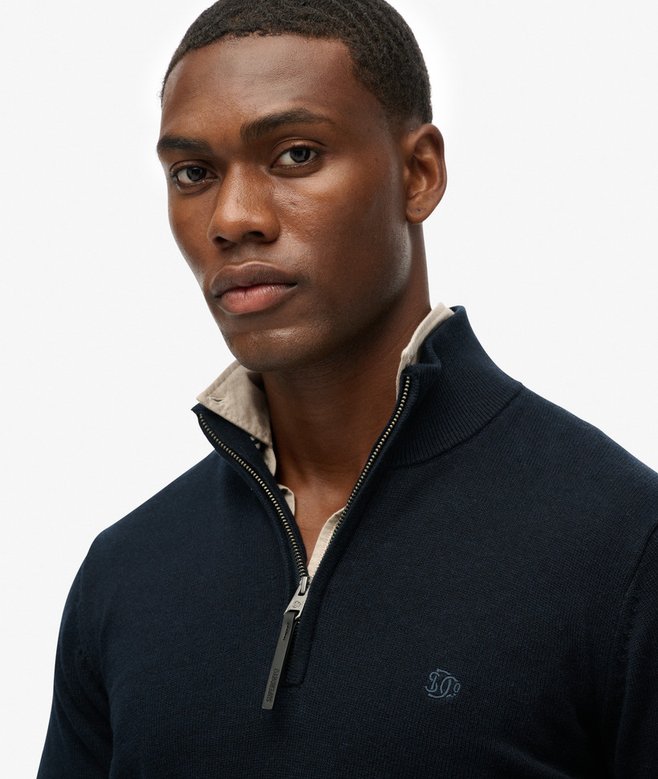 Man wearing a navy blue sweater with a white collar against a plain background