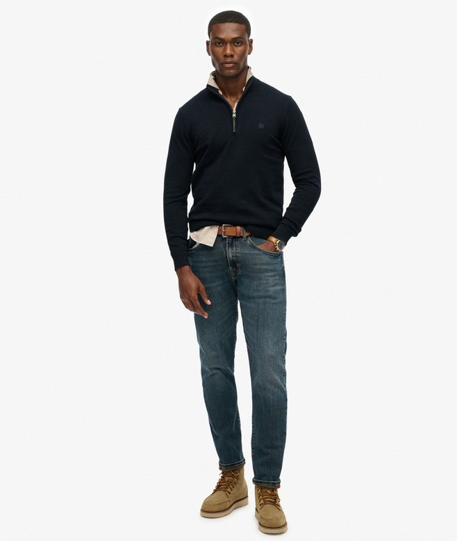 Man wearing a dark blue sweater, jeans, and brown boots on a white background