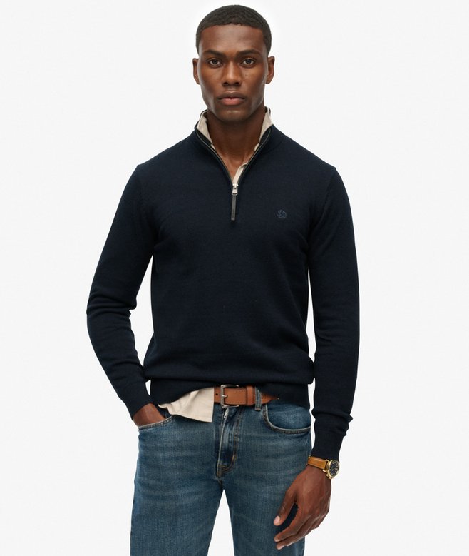 Man wearing a navy quarter-zip sweater and jeans on a white background