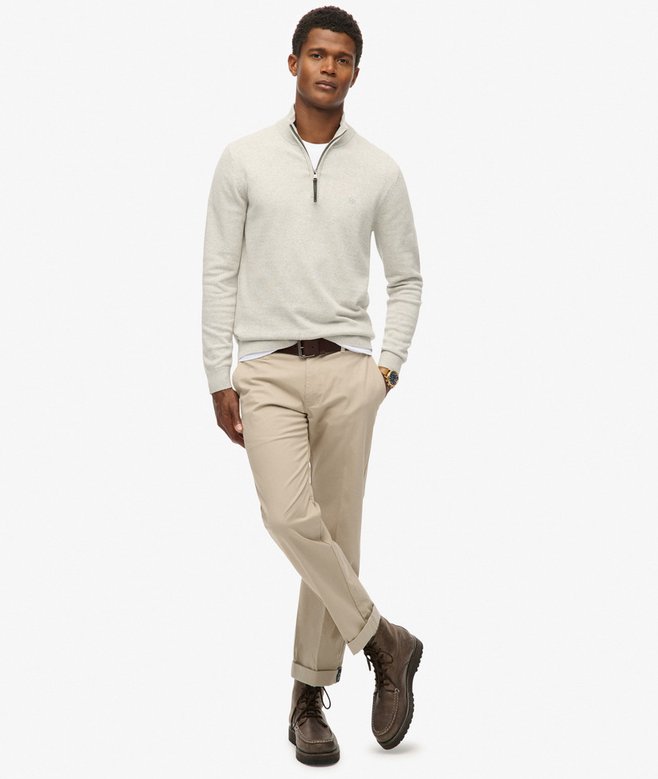 Man wearing a light gray sweater, beige pants, and brown shoes on a white background