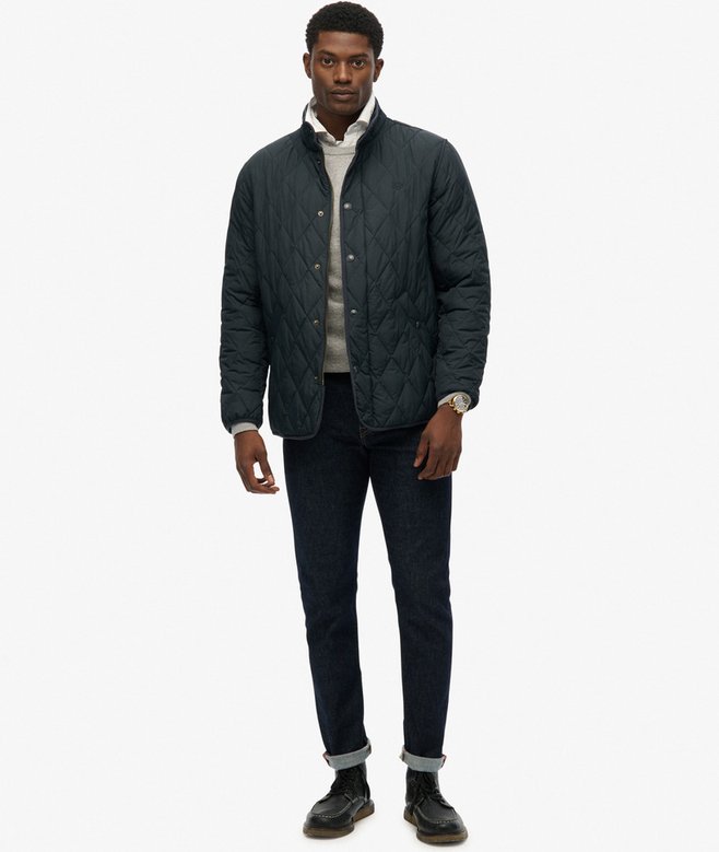 Man wearing a navy quilted jacket over a light shirt with dark pants on a white background