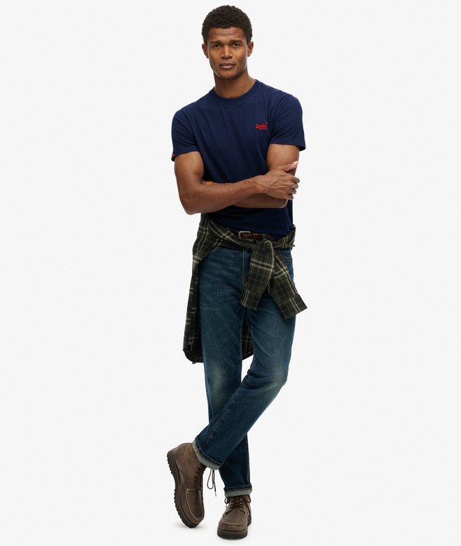 Man wearing a navy t-shirt, blue jeans, and a plaid apron on a white background