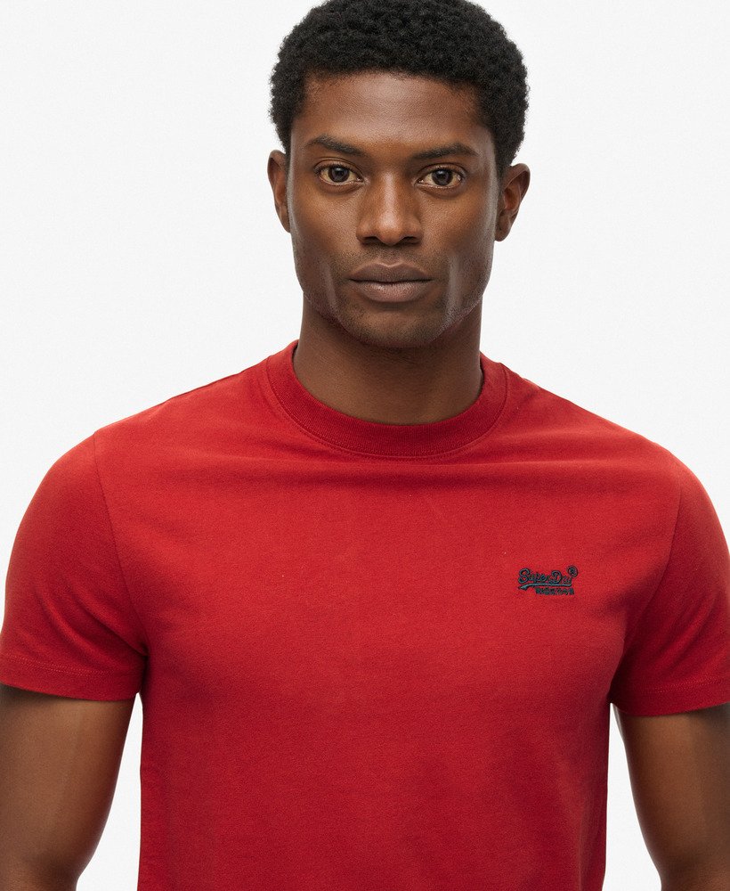 Man wearing a red t-shirt with a small logo on a white background