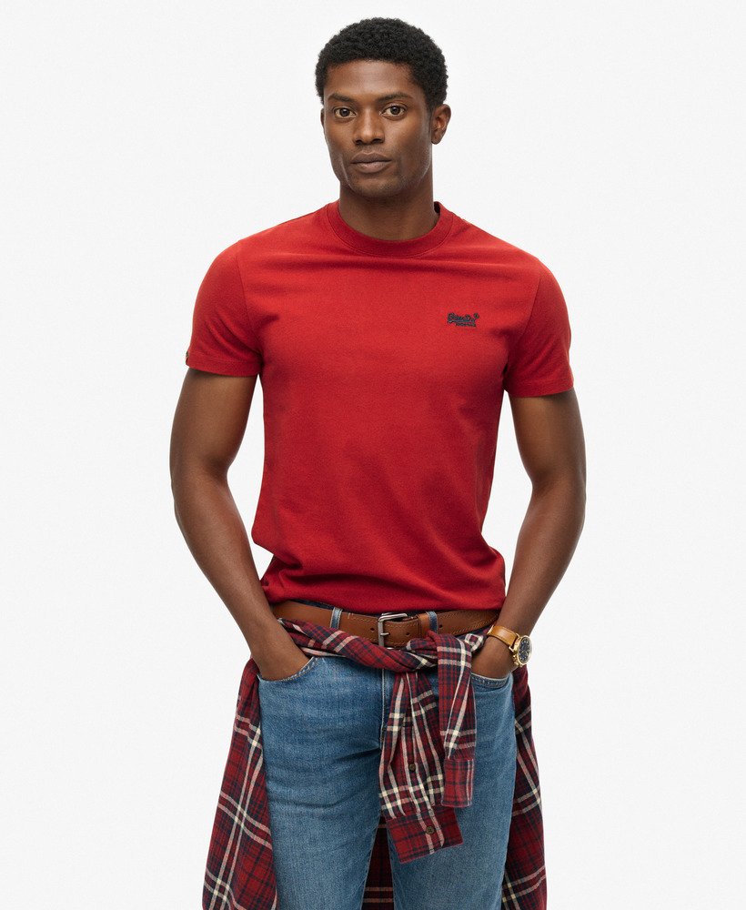 Man wearing a red t-shirt with a plaid shirt over jeans on a white background