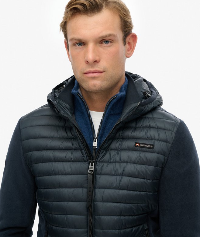 Man wearing a dark blue puffer vest with a visible brand logo on a light gray background