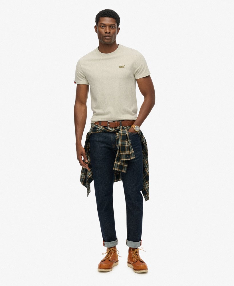 Man wearing a beige t-shirt, dark jeans, and brown boots on a white background