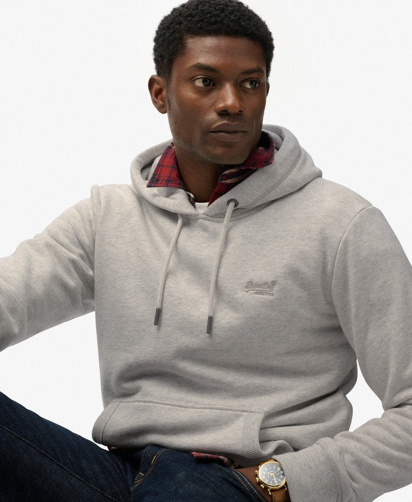 Man wearing a gray hoodie with a brand logo, sitting against a white background