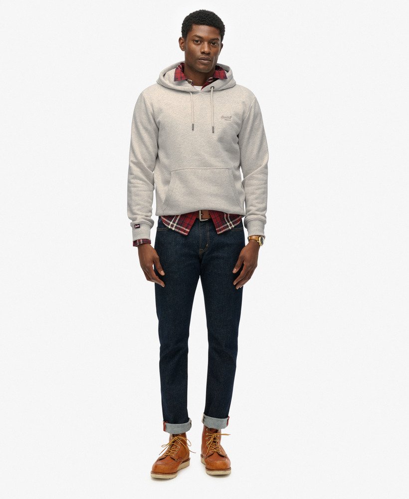 Man wearing a light gray hoodie, plaid shirt, dark jeans, and brown boots on a white background