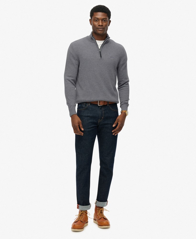 Man wearing a gray sweater, dark jeans, and brown boots on a white background