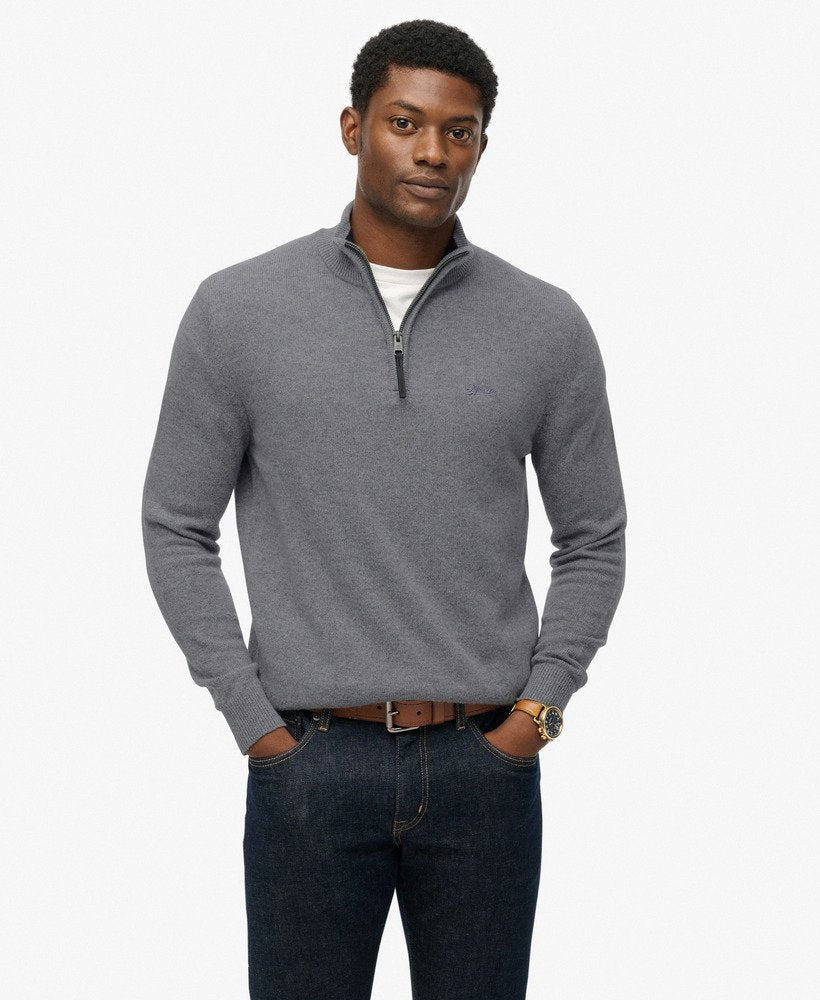 Man wearing a gray quarter-zip sweater and dark jeans on a white background