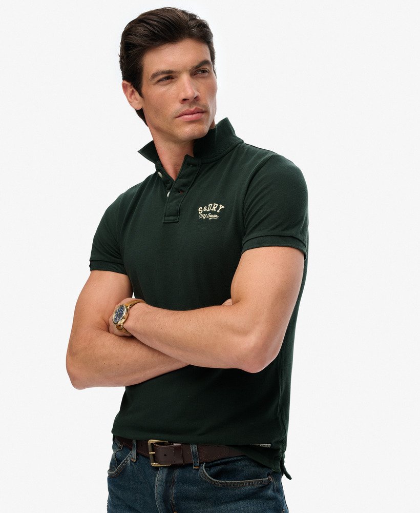 Man wearing a dark green polo shirt with a logo on a white background