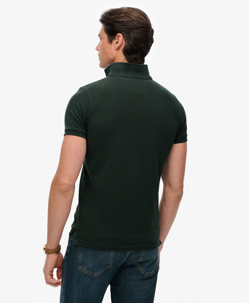 Man wearing a dark green polo shirt and blue jeans on a white background
