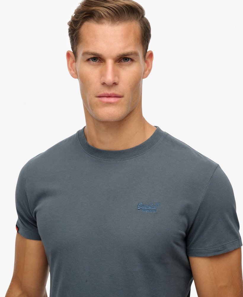 Man wearing a gray t-shirt with a small logo on a light gray background