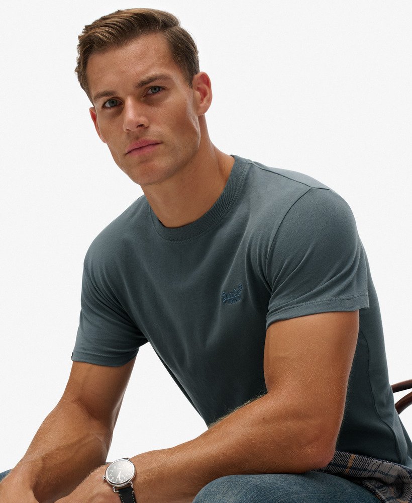 Man wearing a grey t-shirt sitting against a white background