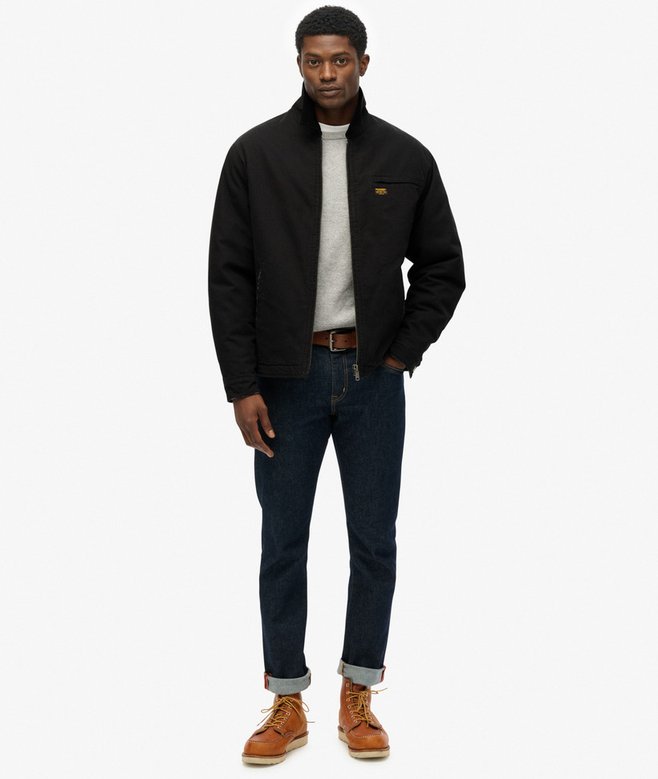 Man wearing a black jacket, white shirt, blue jeans, and brown boots on a white background