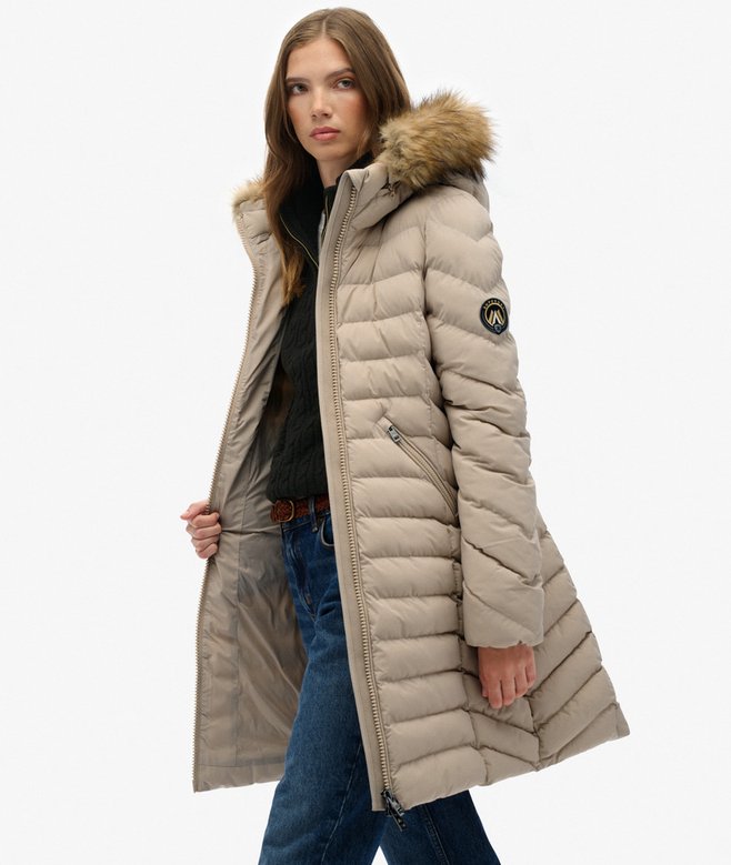 Woman wearing a beige puffer coat with a fur-lined hood on a white background