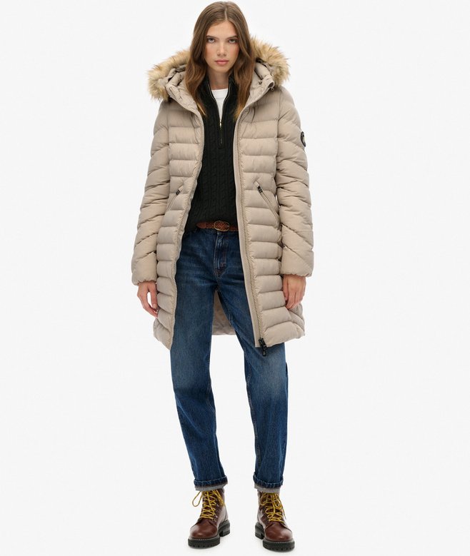 Person wearing a beige puffer coat with fur hood on a white background