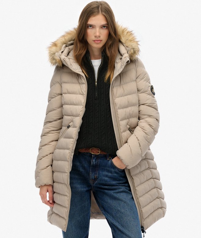 Woman wearing a beige puffer coat with fur hood on a white background