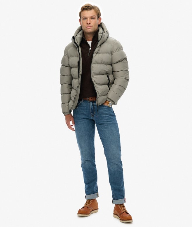 Man wearing a light green puffer jacket, brown shirt, blue jeans, and brown boots on a white background