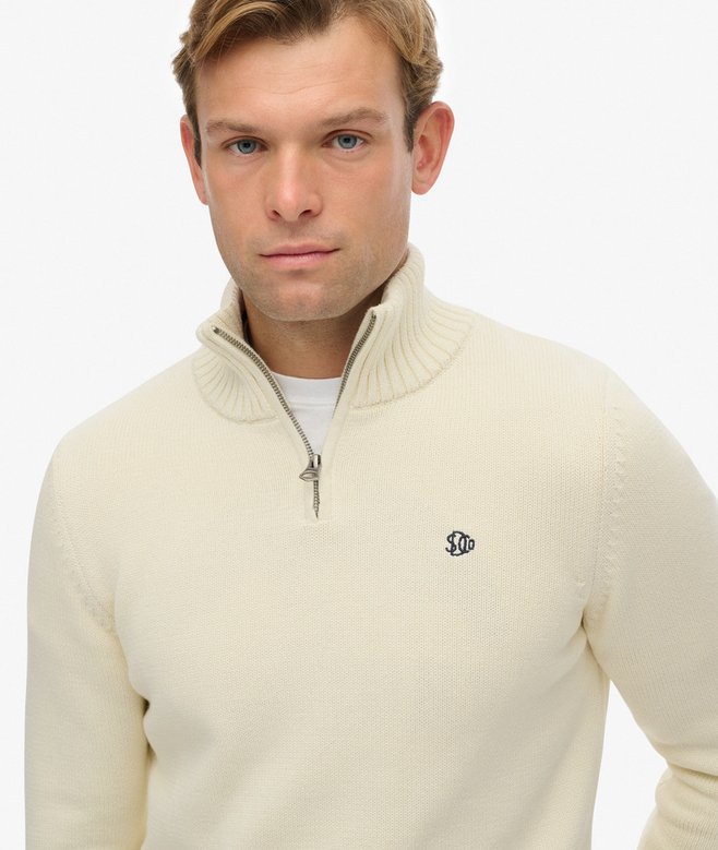 Man wearing a beige half-zip sweater with a logo on a white background