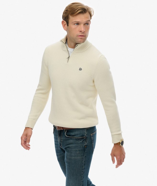 Man wearing a cream half-zip sweater and blue jeans on a white background