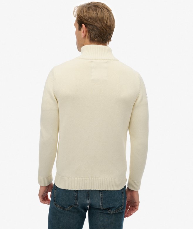 Man wearing a beige sweater and blue jeans on a white background