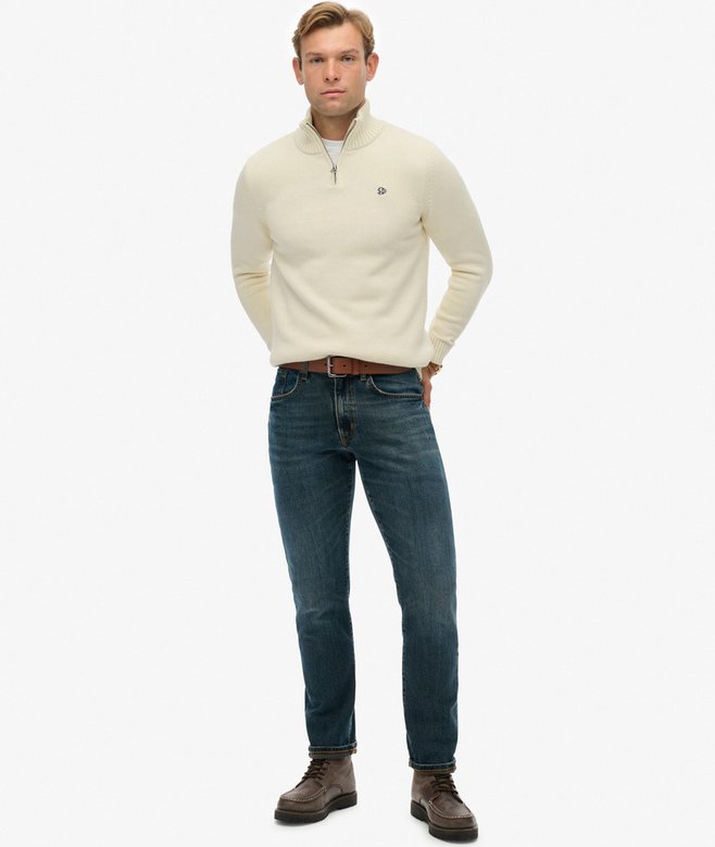 Man wearing a cream sweater and blue jeans on a white background