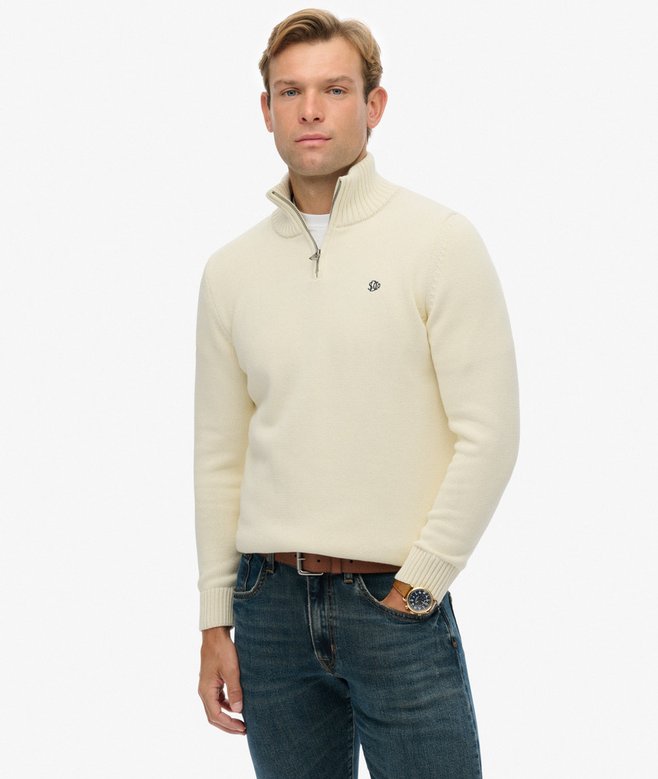 Man wearing a cream half-zip sweater and blue jeans on a white background