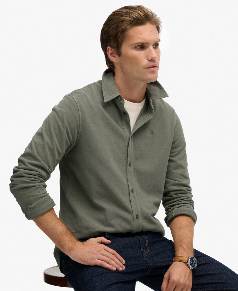 Man wearing a green button-up shirt sitting on a stool against a white background