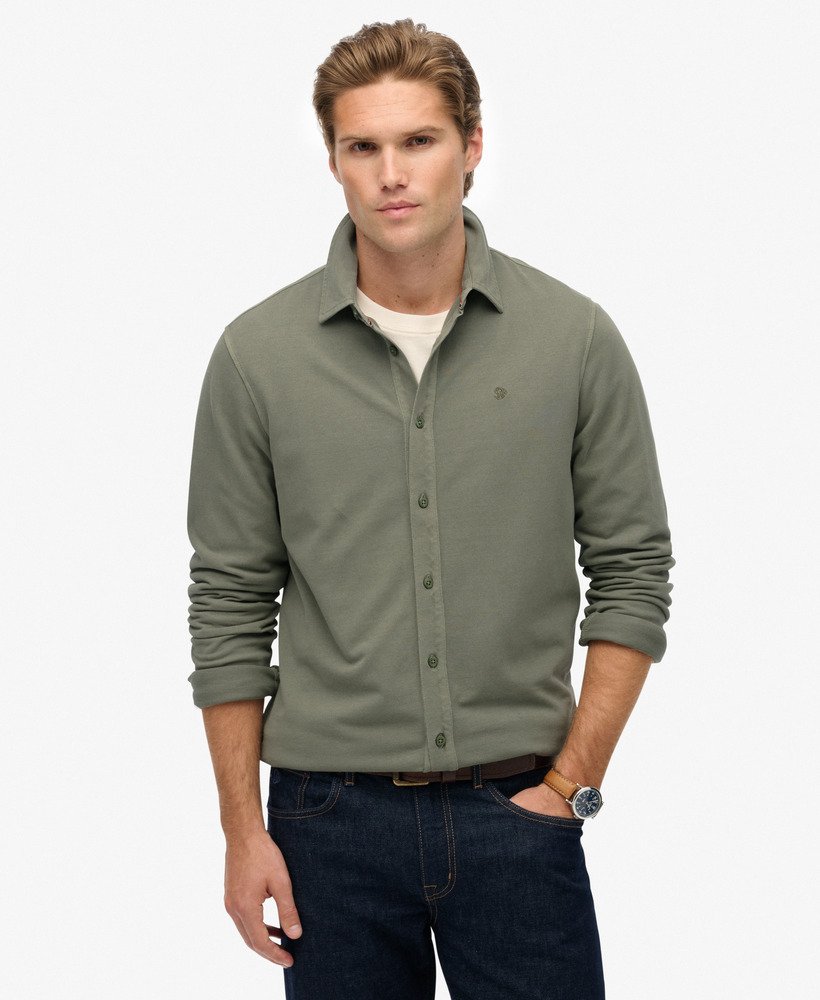 Man wearing a green button-up shirt and dark jeans on a white background