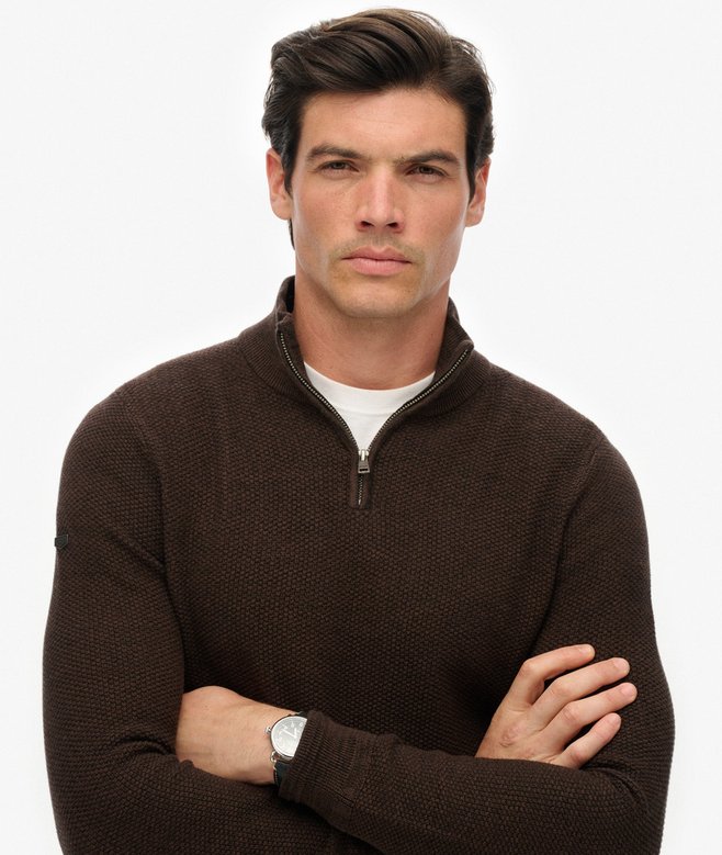 Man wearing a brown quarter-zip sweater with arms crossed on a white background